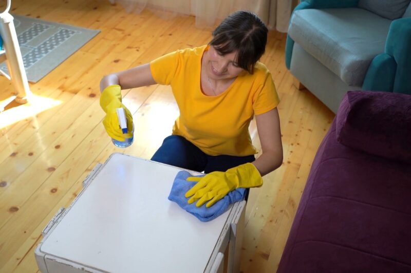 devojka čisti drveni stolčić sa sredstvom i krpom